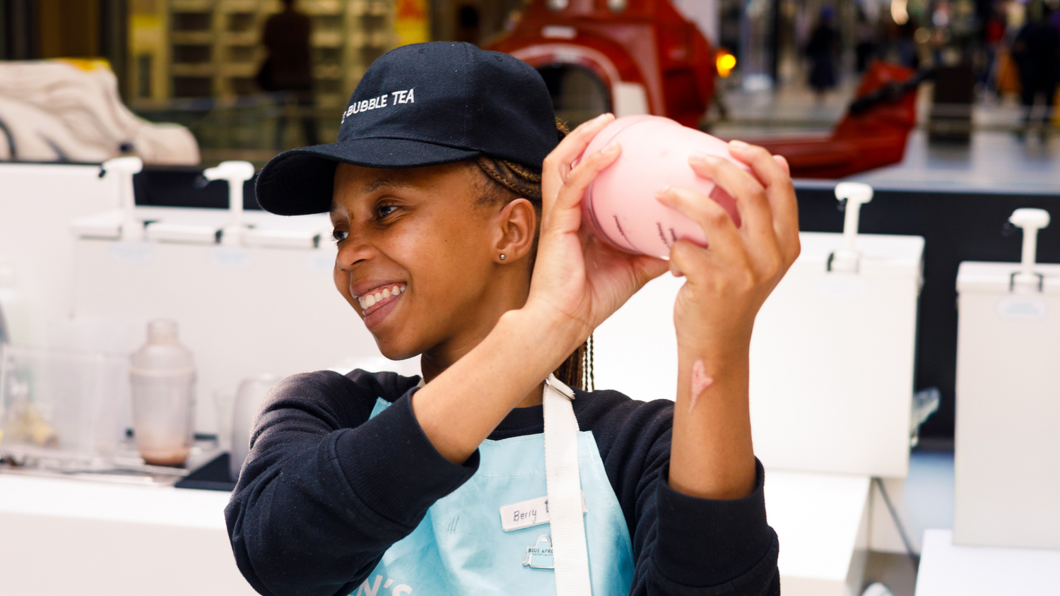 Person wearing a blue apron and cap, holding a pink object in a store setting.